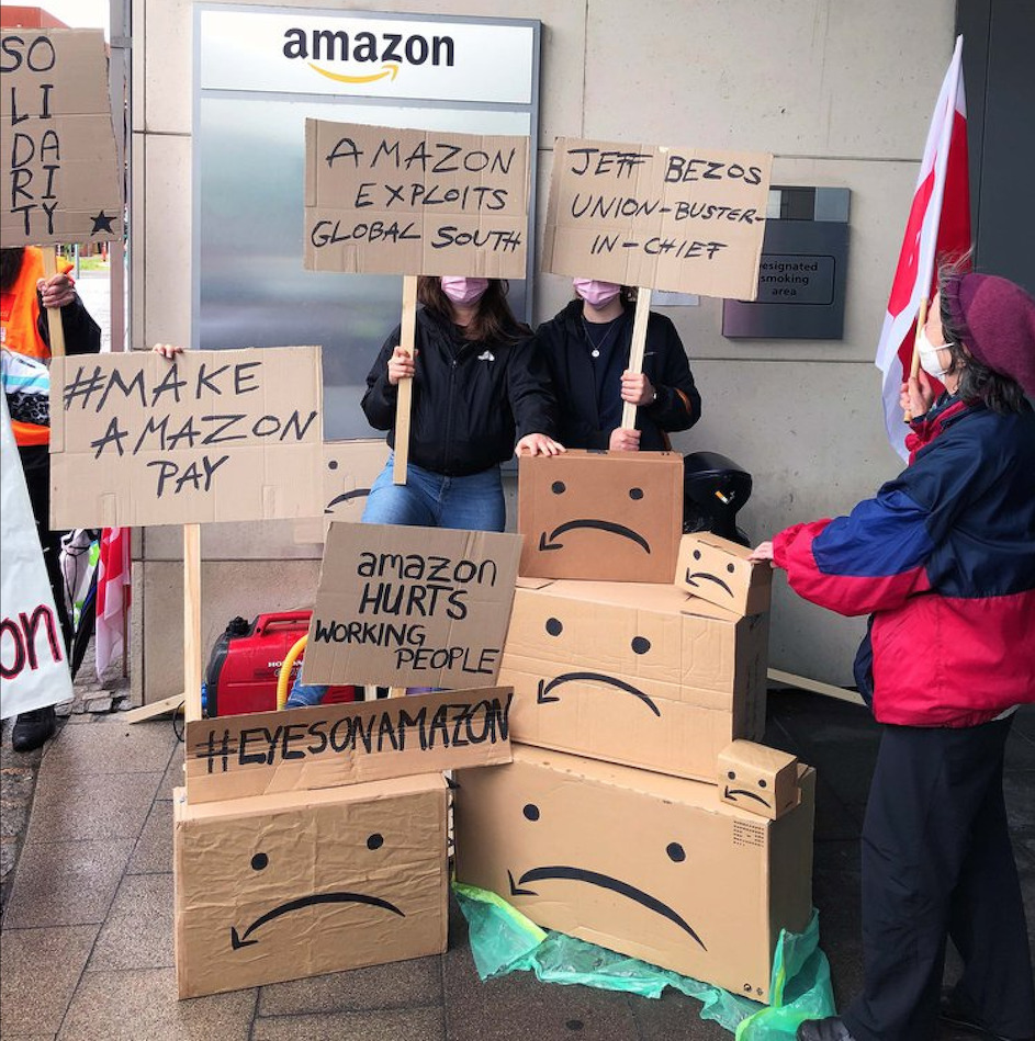 „Jeff Bezos – Union Buster in Chief“ – der Gründer und langjährige Chef ist auch der größte Verhinderer von Mitbestimmung und Betriebsräten. Und dass er kaum Steuern zahlt, auch das sagen die Protestschilder von Beschäftigten aus verschiedenen europäischen Ländern am 26. Mai 2021 vor der Amazon-Europazentrale in Luxemburg © ethecon.org