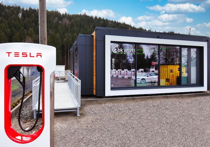 Die E-Tankstelle Füssen mit den Tesla Superchargern und dem Pizzaautomaten spiegelt sich in der Panoramascheibe der bk World Lounge in Füssen, die am 9. Januar 2023 zu Füssen von Schloss Neuschwanstein eröffnet wurde © Pressefoto bk Group AG